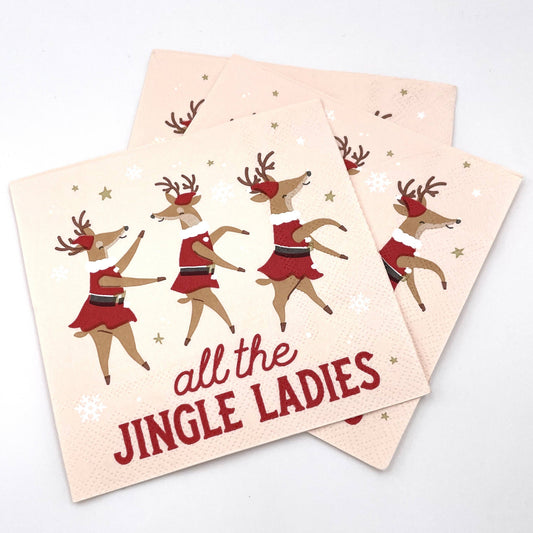 Three square paper napkins with a festive Christmas design, featuring dancing reindeer in red dresses and the text 'all the JINGLE LADIES' on a light beige background, arranged on a white surface.