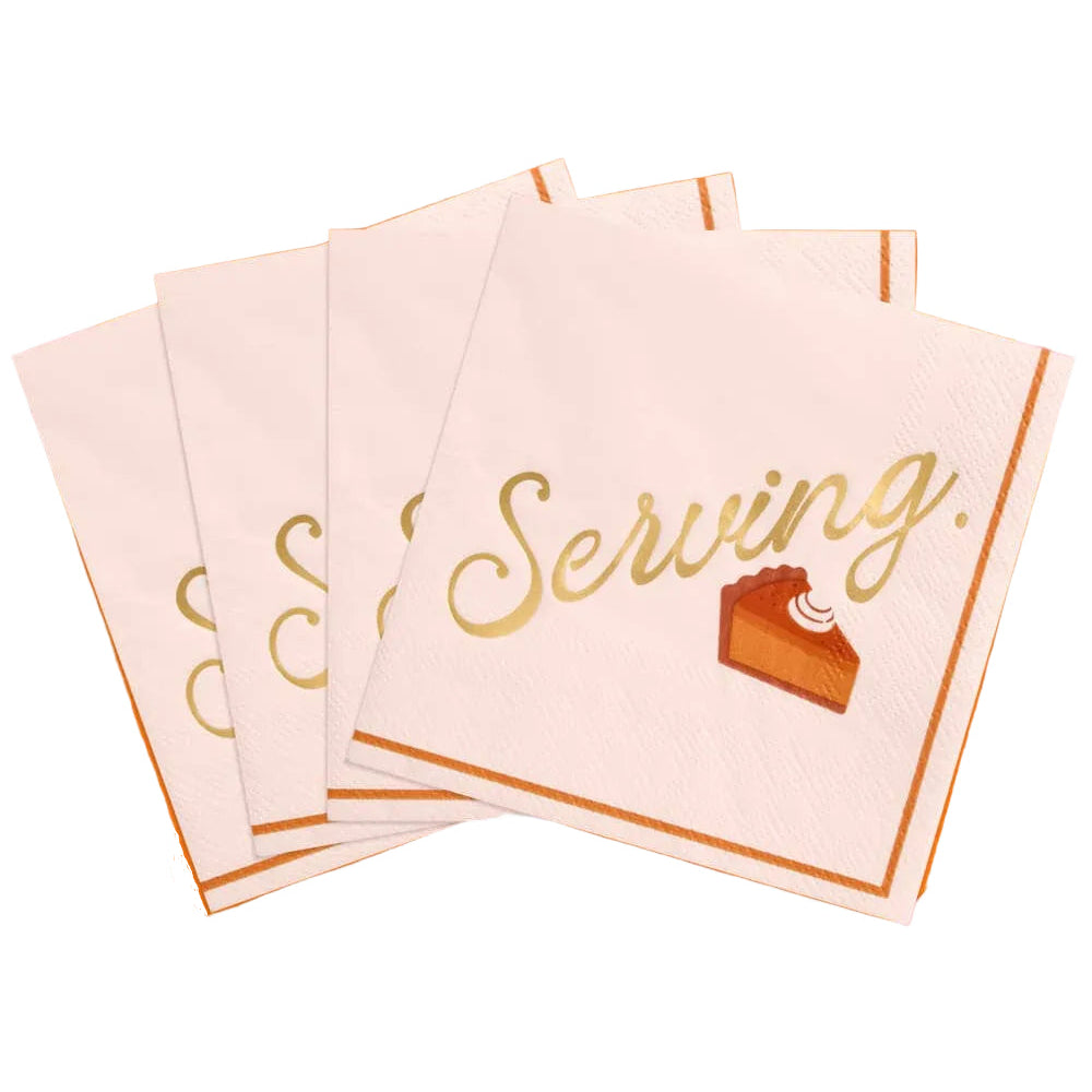 A stack of square white paper napkins with metallic gold foil lettering that reads 'Serving.' and a small slice-of-takeout dessert graphic, arranged on an orange round plate against a pink background.