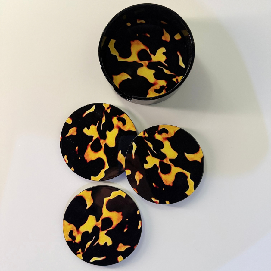 Four oval coasters with a black and yellow tortoiseshell pattern, including one open round container, arranged on a white surface.