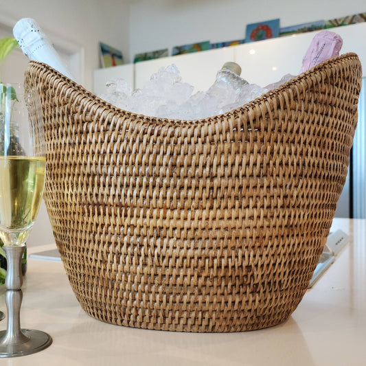 Wicker wine cooler with bottles of champagne on ice, flutes of champagne, and plants in a home setting.