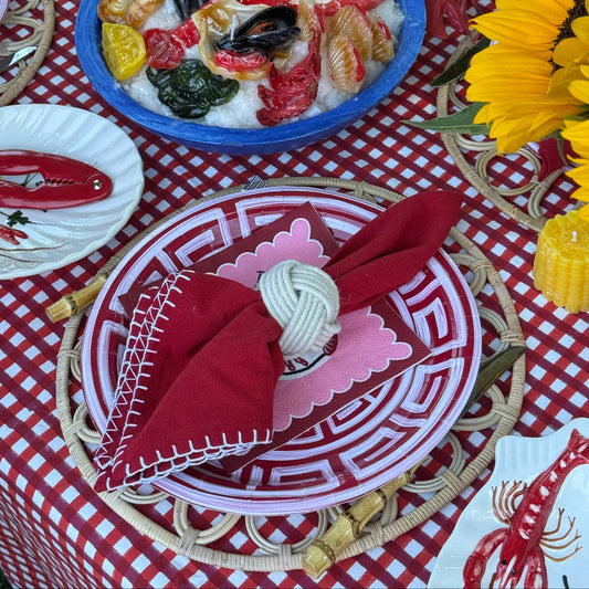 Outdoor dining table setting with a red and white gingham tablecloth, matching plates, red napkins with white stitching, a blue bowl of seafood, and large yellow sunflowers.