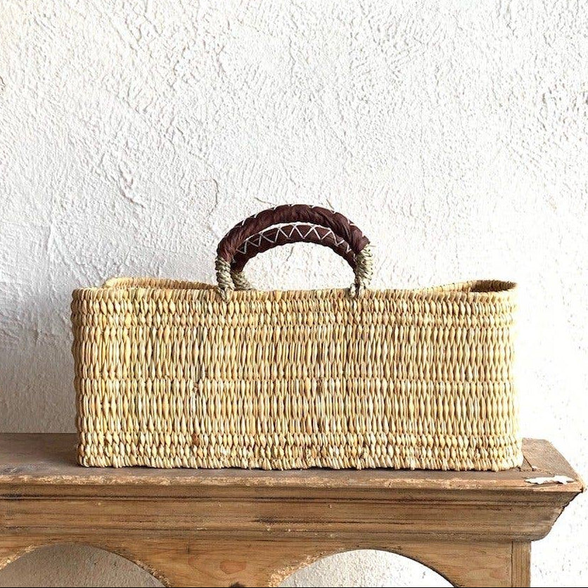 Woven basket with handles on a wooden surface against a white wall