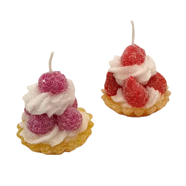 two mini dessert-shaped candles with white frosting swirls, sugar-coated berries, and yellow bases on a plain white background.