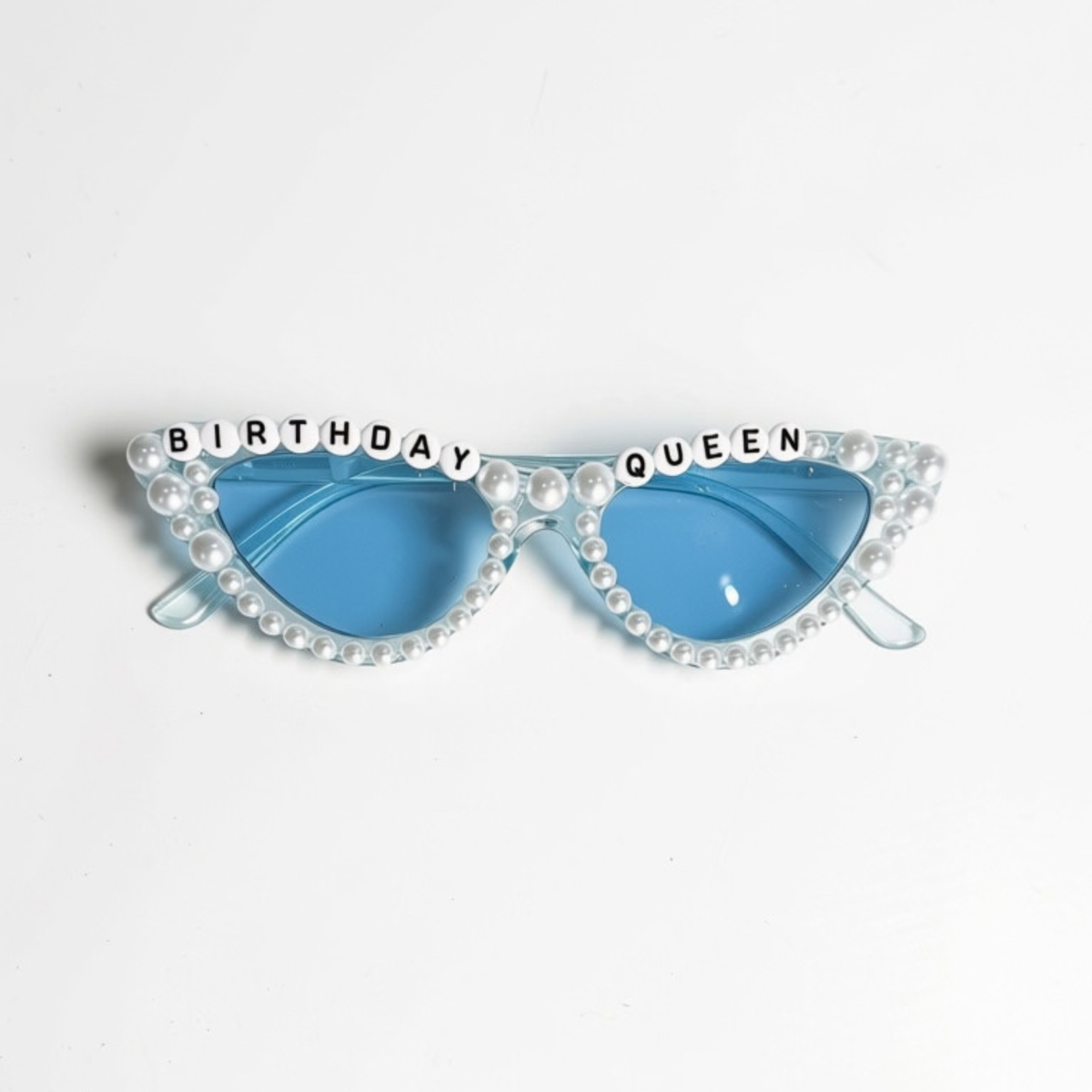 Light blue cat-eye sunglasses with white faux pearl trim and black letter beads spelling 'BIRTHDAY QUEEN' across the top, shown on a plain white background.