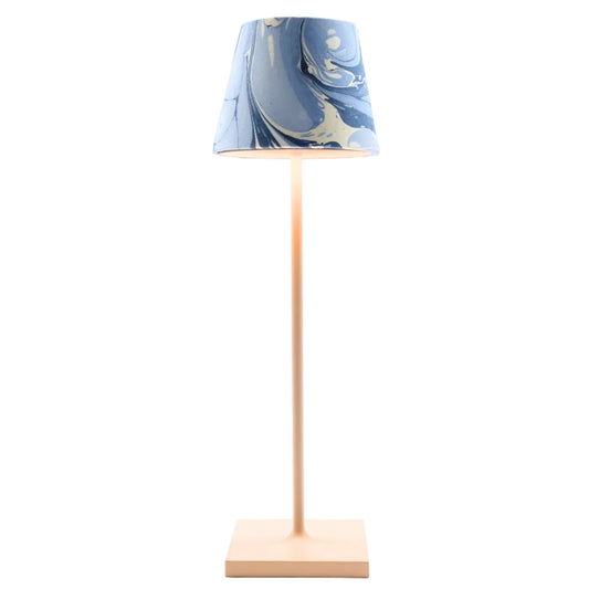A modern table lamp with a tall, slender light wood stand and a square base, featuring a tapered lampshade with a blue and white marbled swirl pattern, shown against a plain white background.