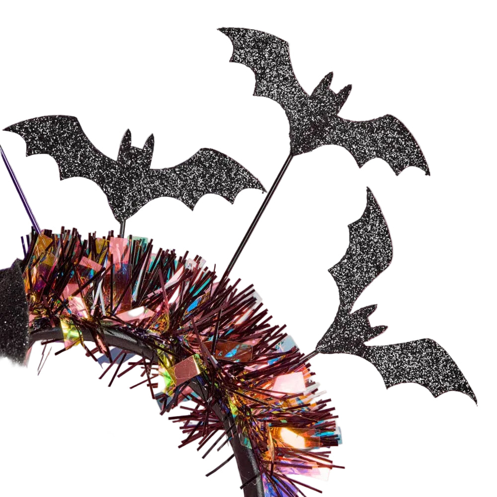 Black glitter bat cutout decorations on a black wire frame, styled with iridescent tinsel and warm fairy lights against a pink and lavender background.