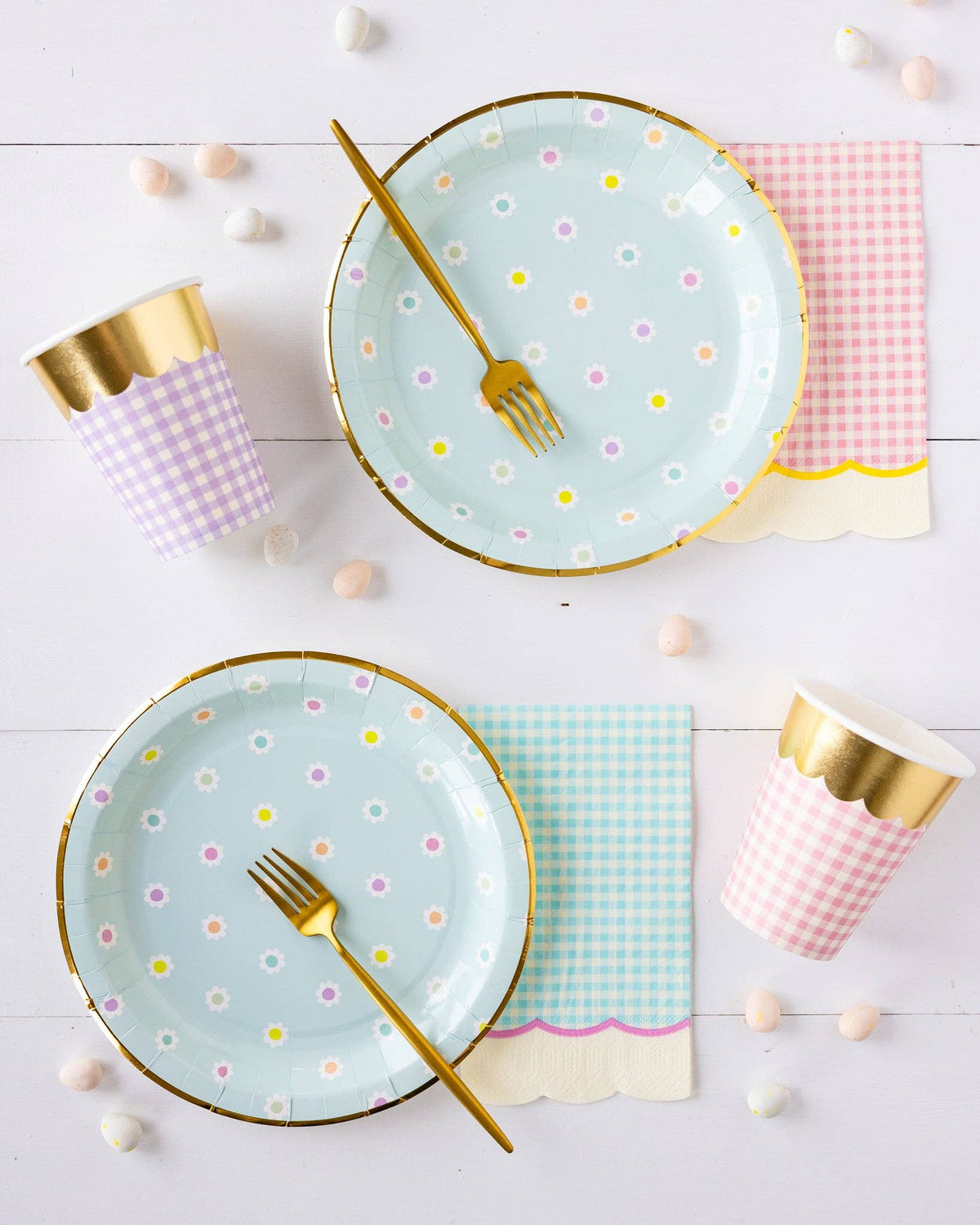 Polka dot plates with gold rims, gold forks, and checkered cups on a white wooden surface.