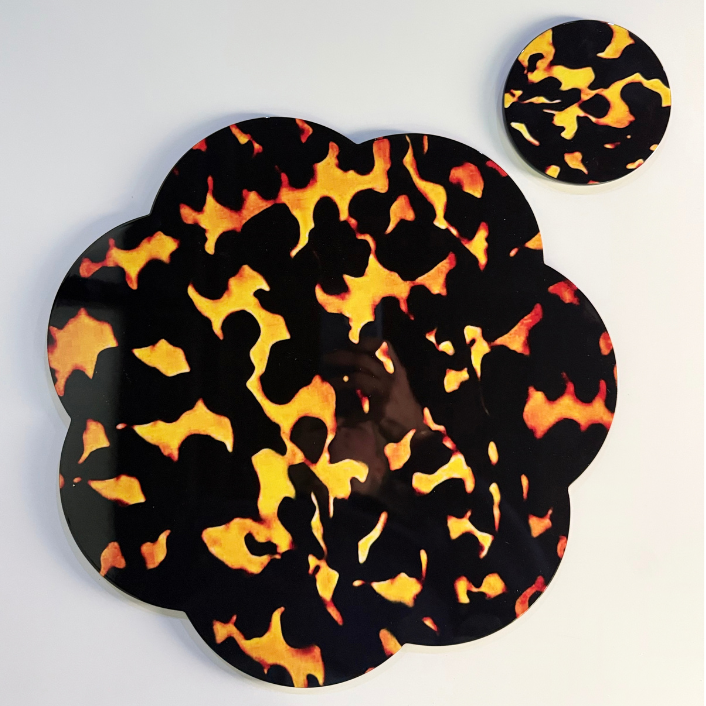 A scalloped circular placemat with a black, orange, and yellow flame pattern, shown alongside a smaller matching coaster