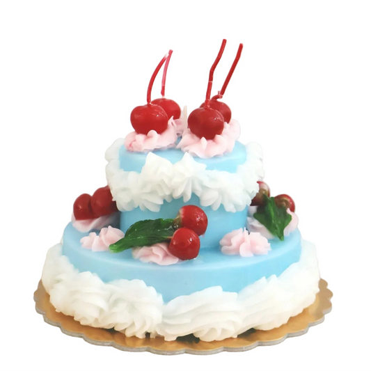 Two-tiered cake with blue frosting, white flowers, and red cherries on a textured surface.