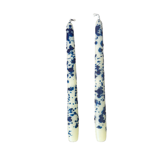 Two long taper candles with a blue and white splatter pattern, standing upright against a plain white background.