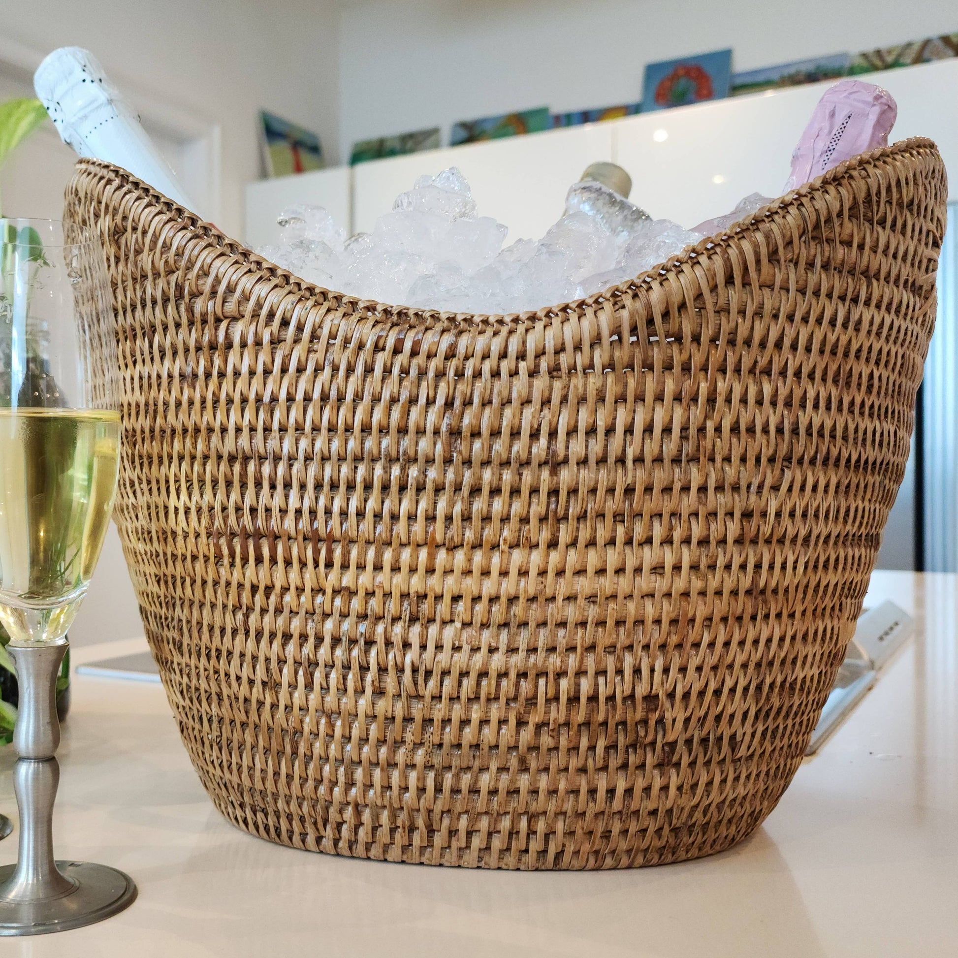 Wicker wine cooler with bottles of champagne on ice, flutes of champagne, and plants in a home setting.