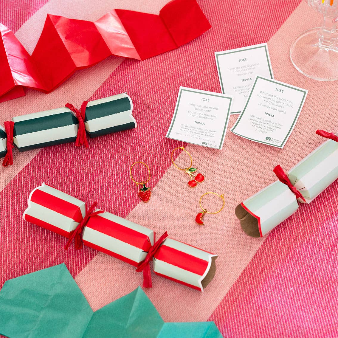 Christmas cracker with red and white striped paper on a pink tablecloth.