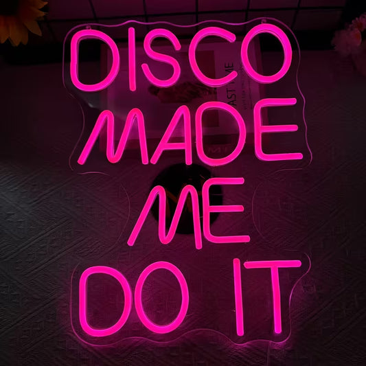 Neon sign with pink text 'DISCO MADE ME DO IT' on a dark background