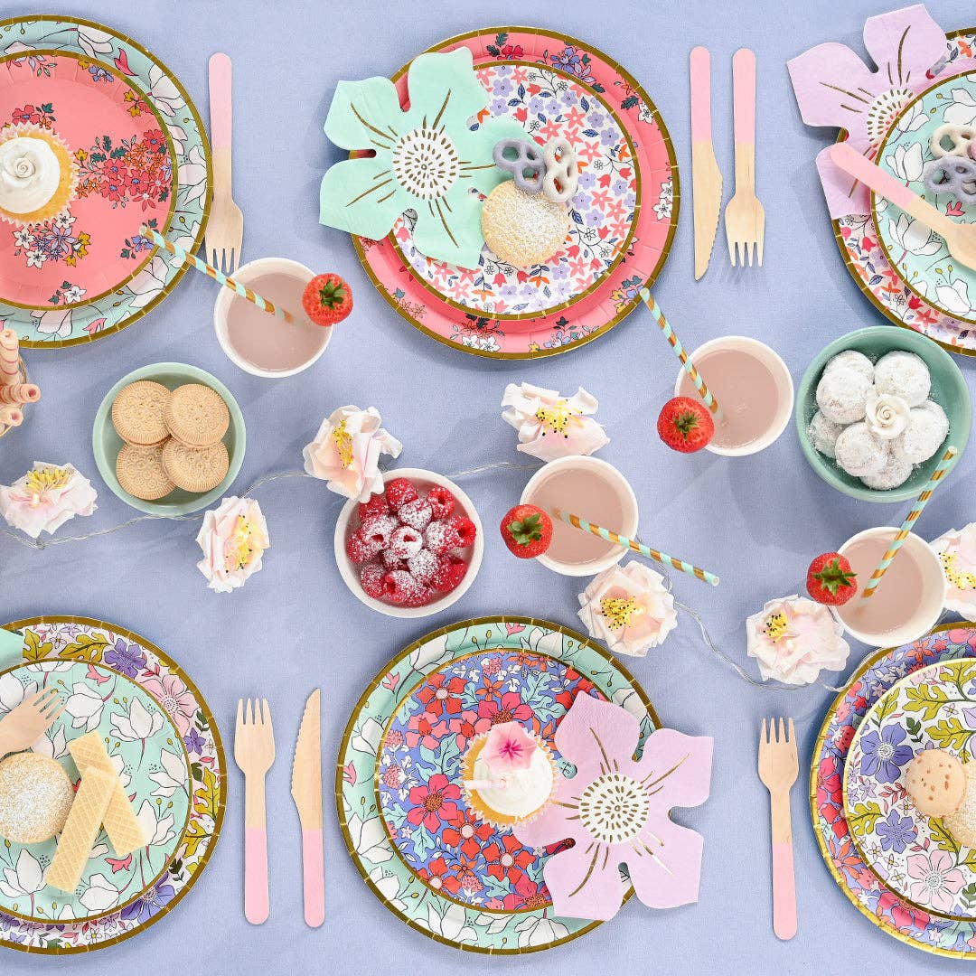 Colorful table setting with floral plates, cups, and utensils on a light purple background.