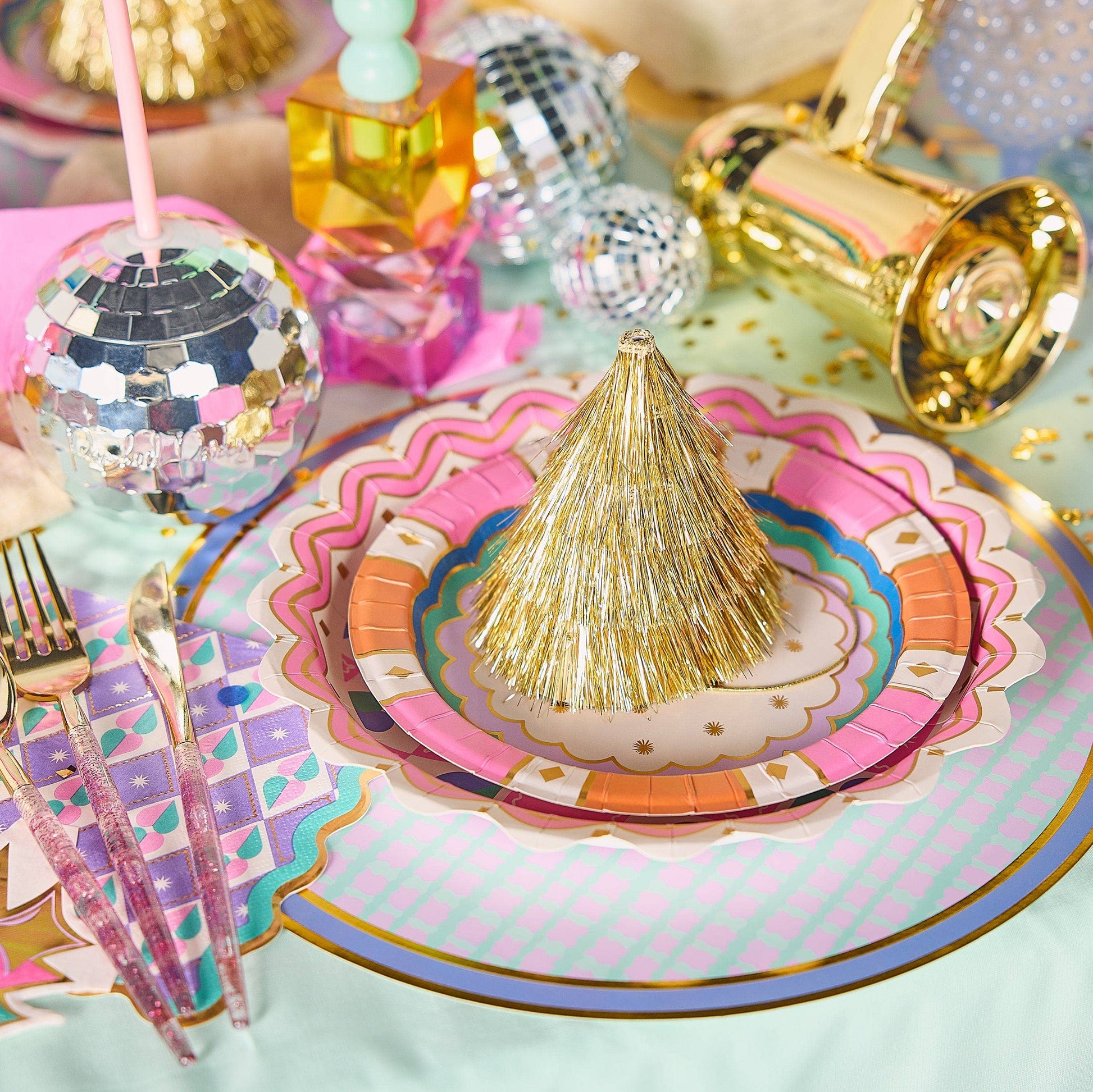 Decorative table setting with colorful plates, gold accents, and party favors.