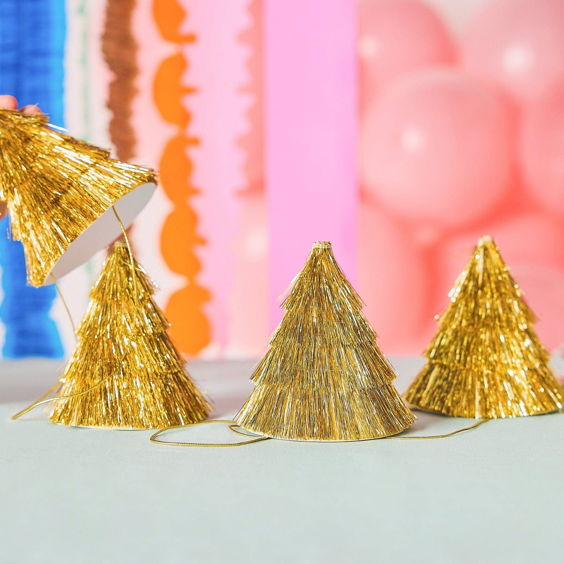 Gold tinsel party hats with colorful balloons in the background