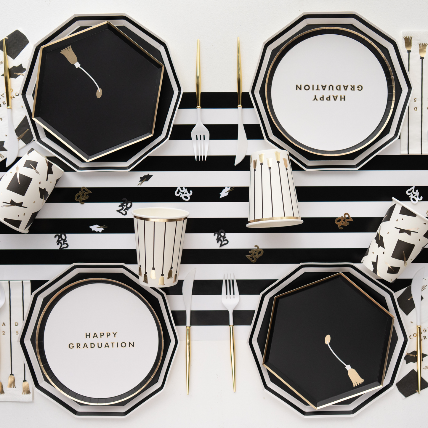 Graduation-themed table setting with black and white plates, gold cutlery, and decorative items on a striped background.