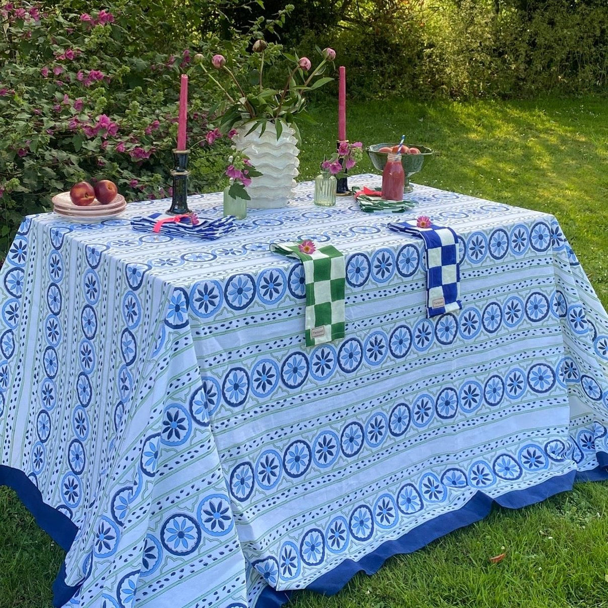 Outdoor table setting with a blue and white patterned tablecloth in a garden.