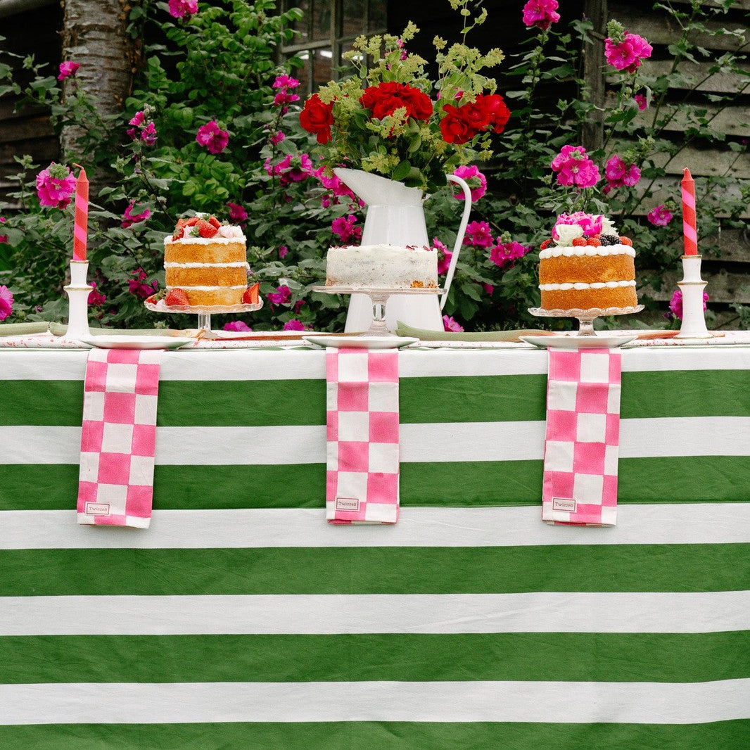 Outdoor setting with a table covered in a green and white striped tablecloth, decorated with cakes and flowers.