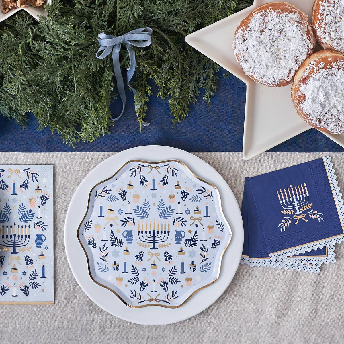 Decorative plate with Menorah design, blue napkin, and greenery on a table.
