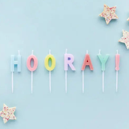 Colorful 'HOORAY!' letter candles on a light blue background 