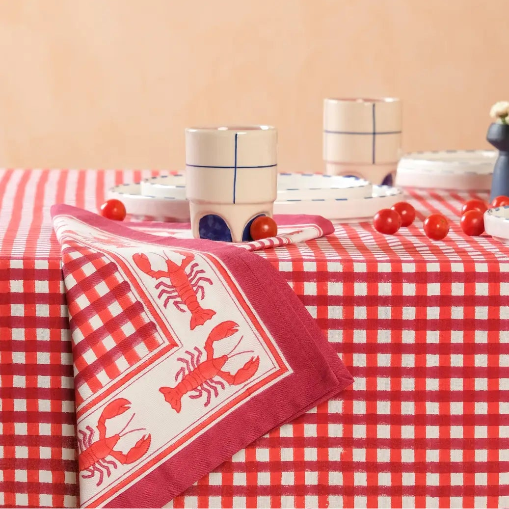 Table with a red and white checkered tablecloth, lobster-themed napkin, and decorative items on a peach background.