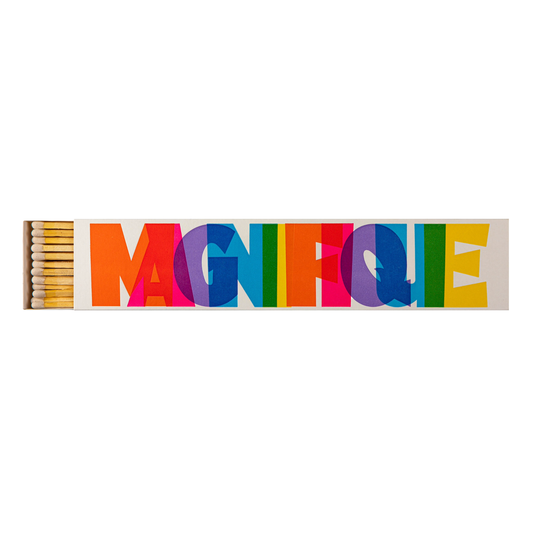 A long rectangular box of matches with a colorful printed lid spelling the word "MAGNIFIQUE" in large overlapping letters. The matches inside are light wood with yellow tips.