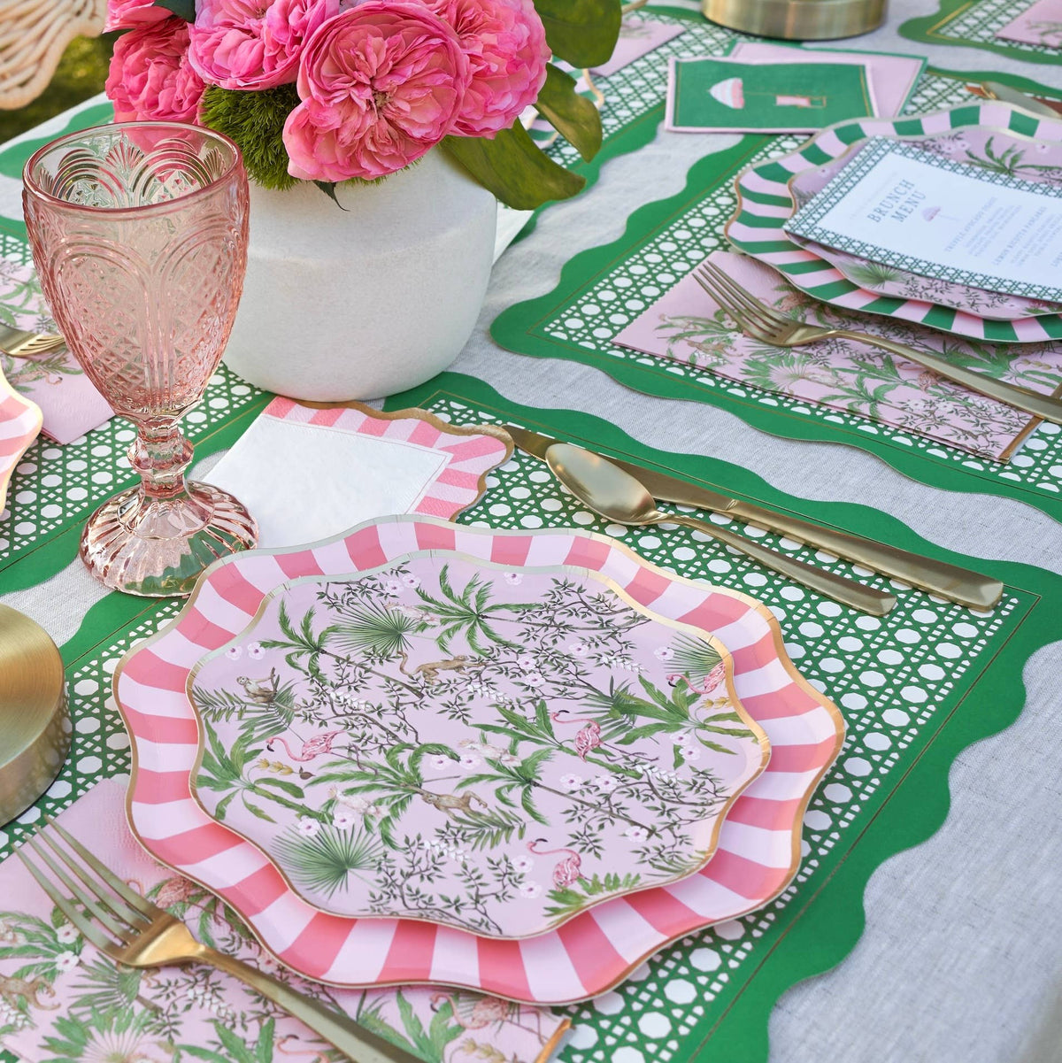 Decorative table setting with floral plates, pink glasses, and a green and white tablecloth.