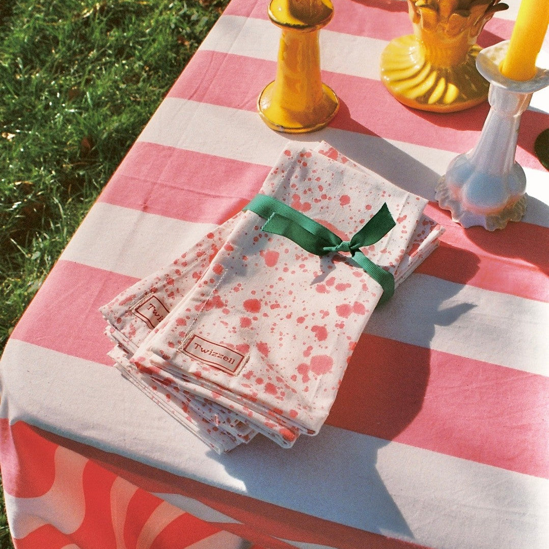 Table setting with pink and white striped tablecloth, floral napkins, and colorful candles outdoors.