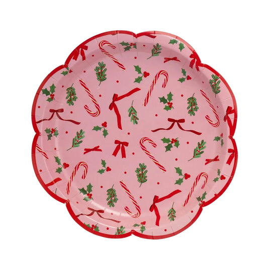 A scalloped paper plate with a festive Christmas pattern featuring red candy canes, green holly leaves, red bows, and red berries on a light pink background.