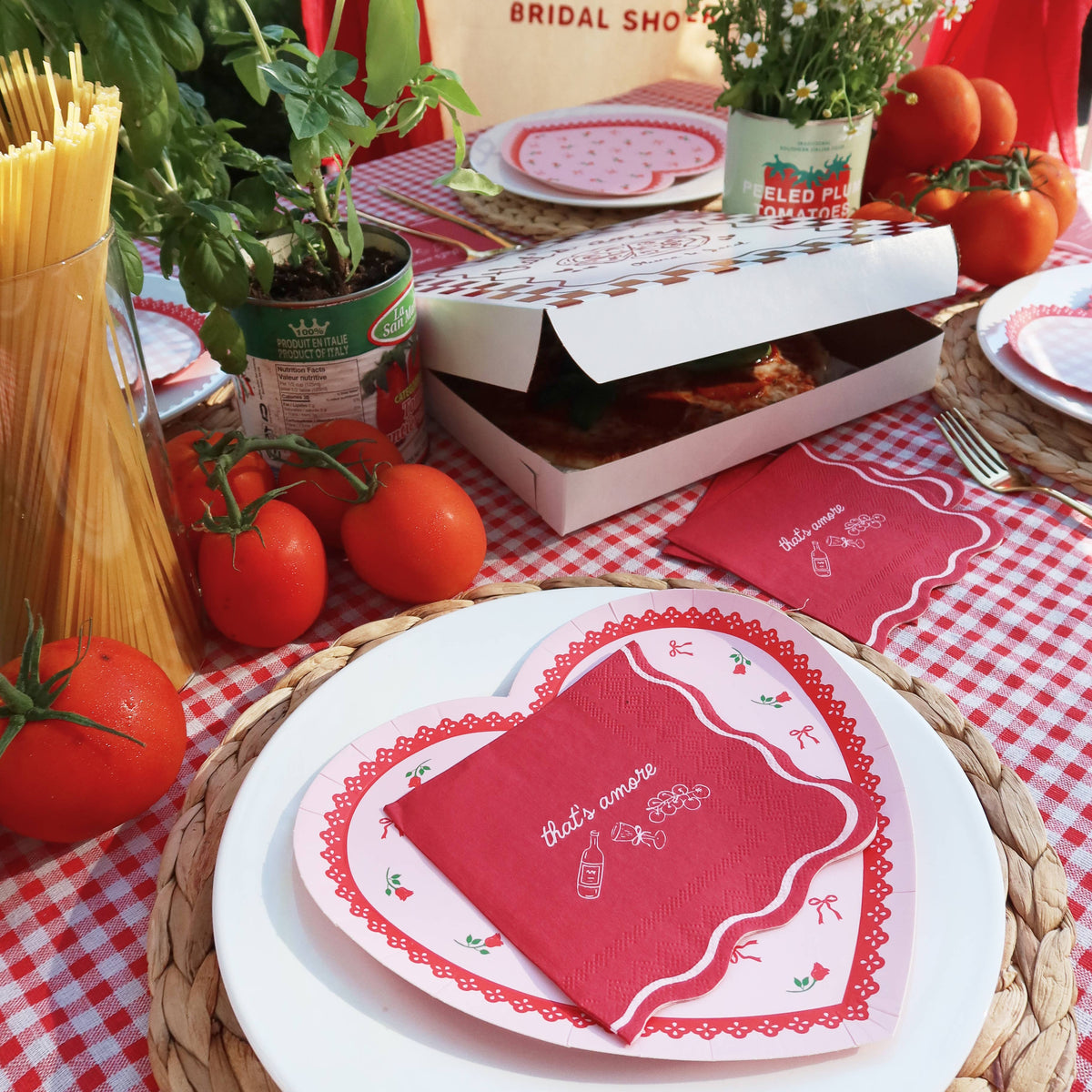 Table setting with red and white checkered tablecloth, heart-shaped plates, and a box of pizza.