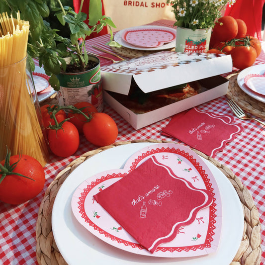 Table setting with red and white checkered tablecloth, heart-shaped plates, and a box of pizza.