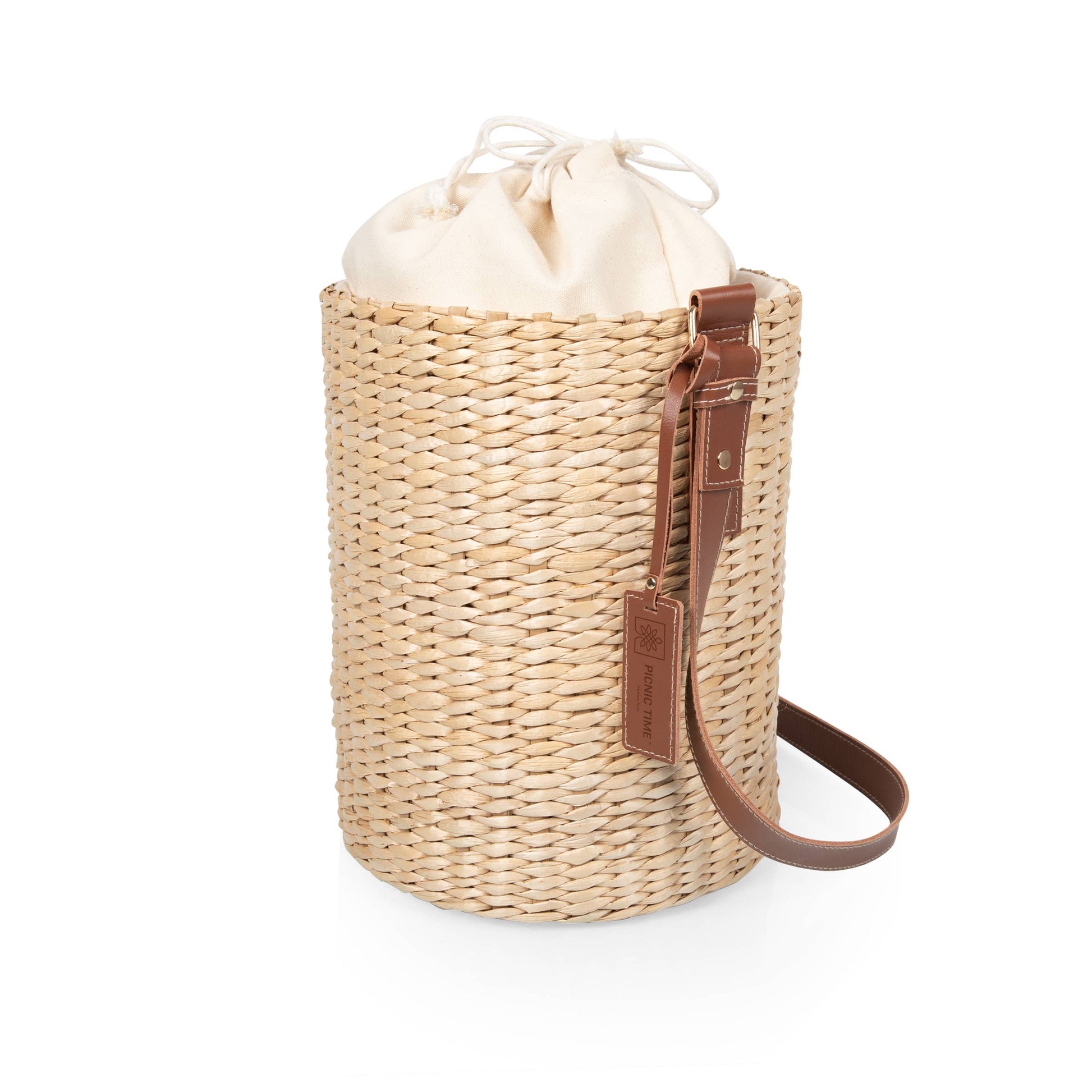 A natural woven straw cylindrical tote bag with a brown leather strap and a cream-colored drawstring pouch on top, shown on a plain white background.