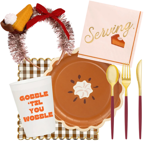 A Thanksgiving tableware set arranged on a white background, including a brown paper plate with pie graphics, a white paper cup with orange text reading 'GOBBLE 'TIL YOU WOBBLE,' gold-handled silverware, a pink napkin with gold script and a pie illustration, a brown-and-white checkered tray, and a tinsel wreath with a red bow and a small pie decoration.