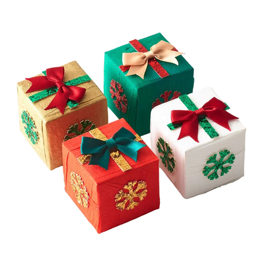 Four small decorative gift boxes arranged on a white background, each with a ribbon bow and holiday snowflake decoration. The boxes are gold, green, red, and white, with red, green, and gold ribbon accents.